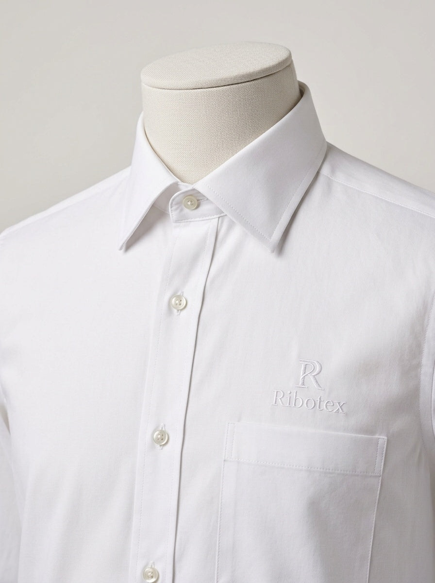 A white long-sleeve button-down dress shirt with a pointed collar and a chest pocket, displayed on a mannequin torso. The brand name 'Ribotex' is subtly embroidered in tonal white on the left chest pocket.